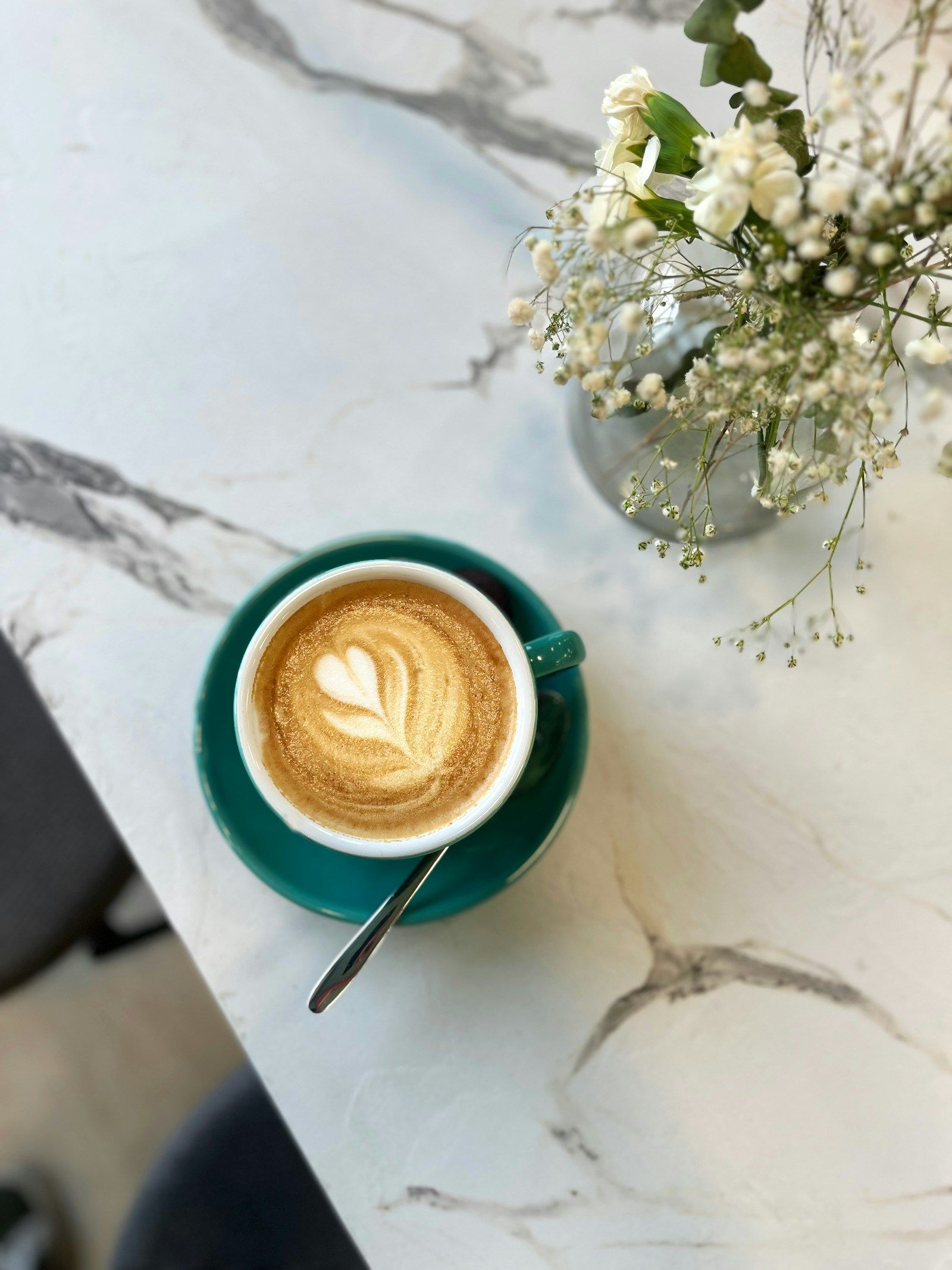 Mermer masada bir fincan latte ve küçük bir vazoda beyaz çiçekler