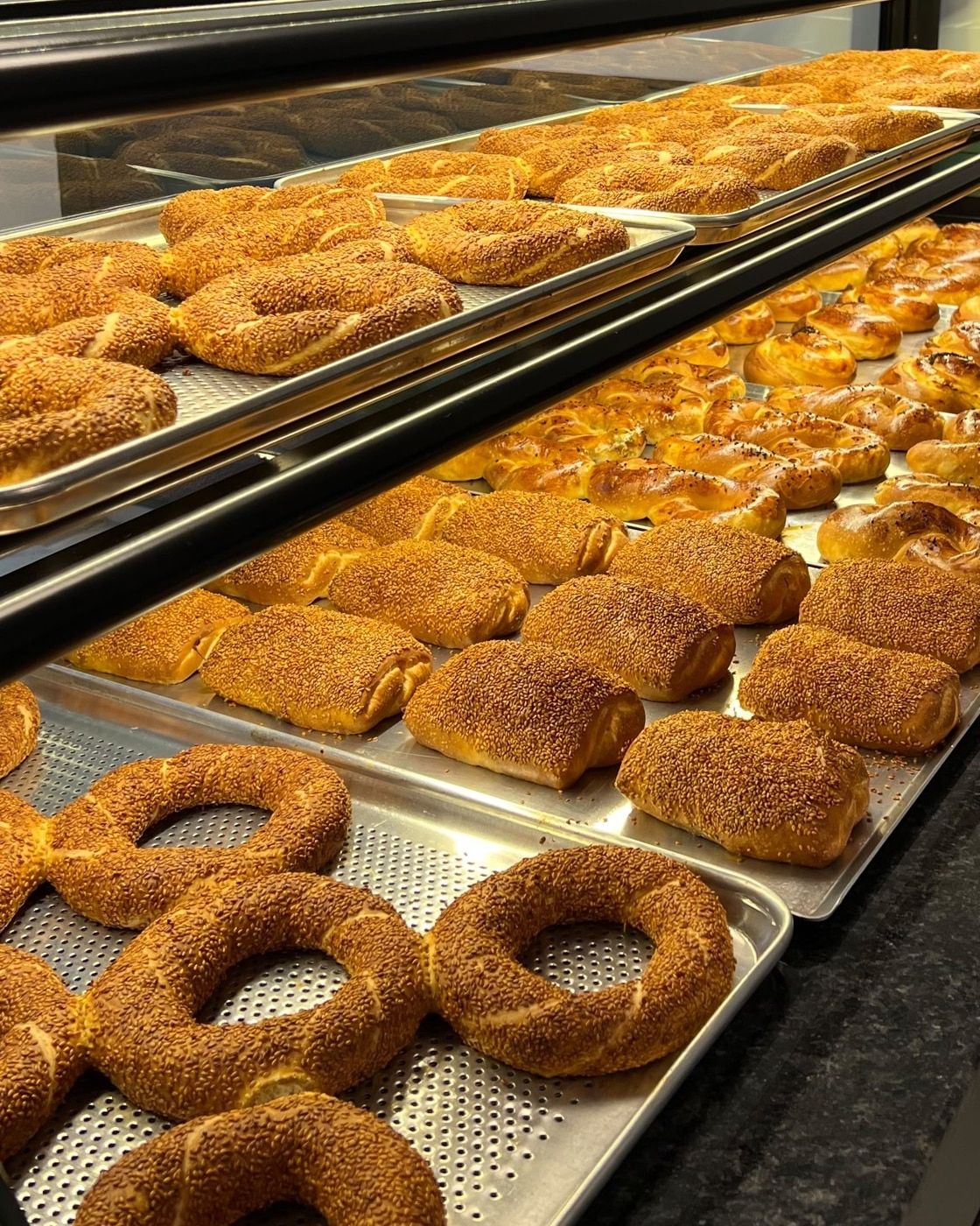 Molla Patisserie tezgâhında tepsilerde simitler, susamlı poğaçalar ve çörekler
