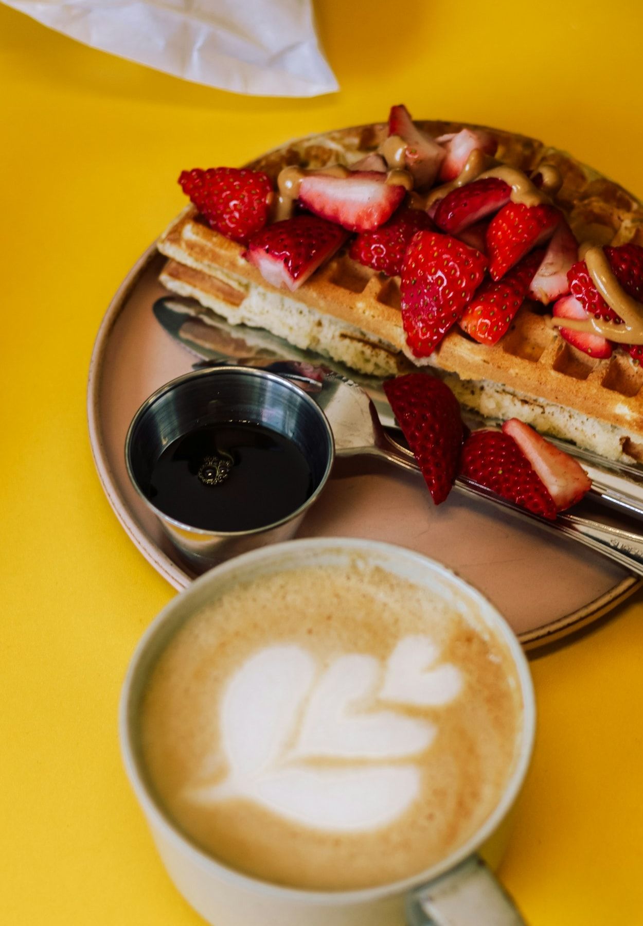 Sarı masada çilekli waffle ve bir fincan latte